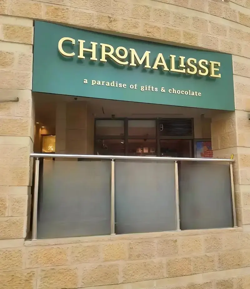 Rótulo iluminado verde oliva con letras halo doradas en un nicho de edificio — ejemplo de retroiluminación halo con efecto de brillo en la pared