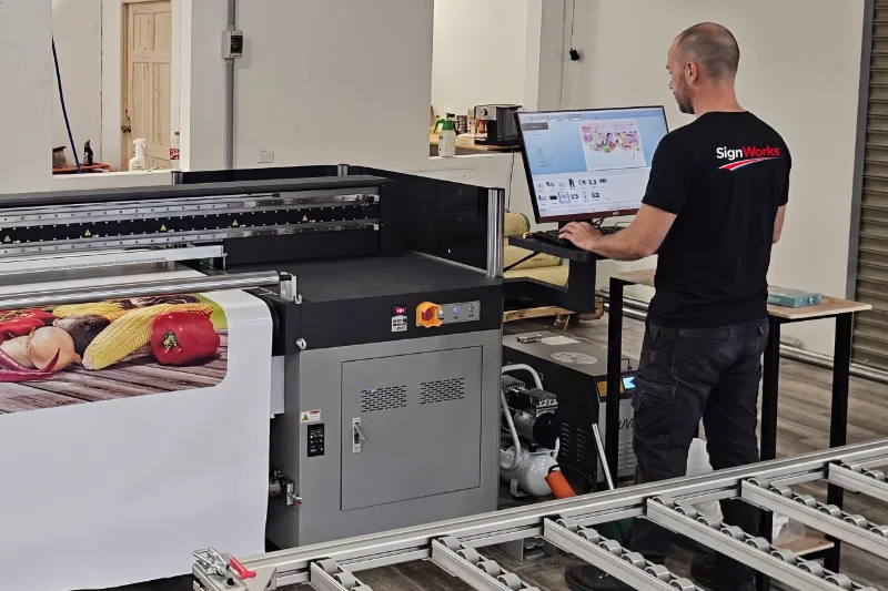 Operator at the control screen of a large-format UV printer while a banner prints, SignWorks Costa Rica