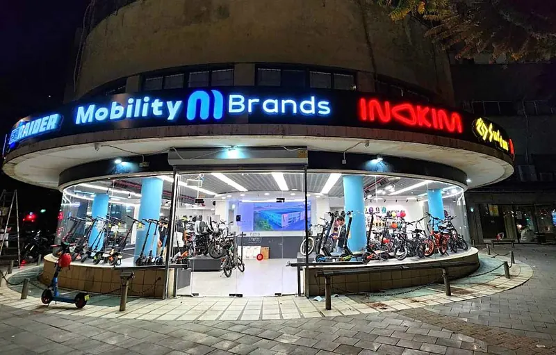 Illuminated sign band with seven brand names curving around a round showroom facade at night