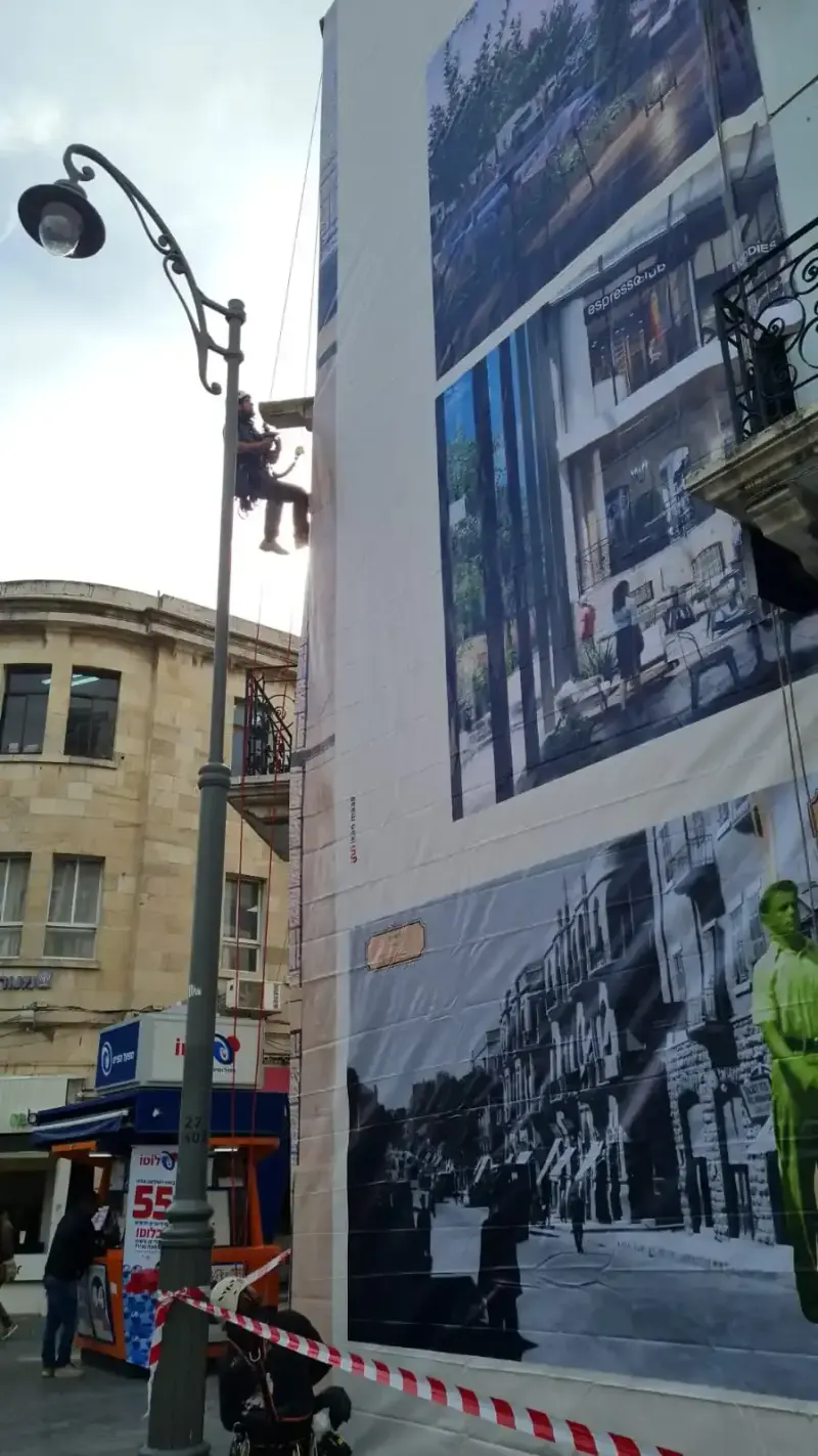 Installer on rope access fixing a large printed poster to the upper face of a building